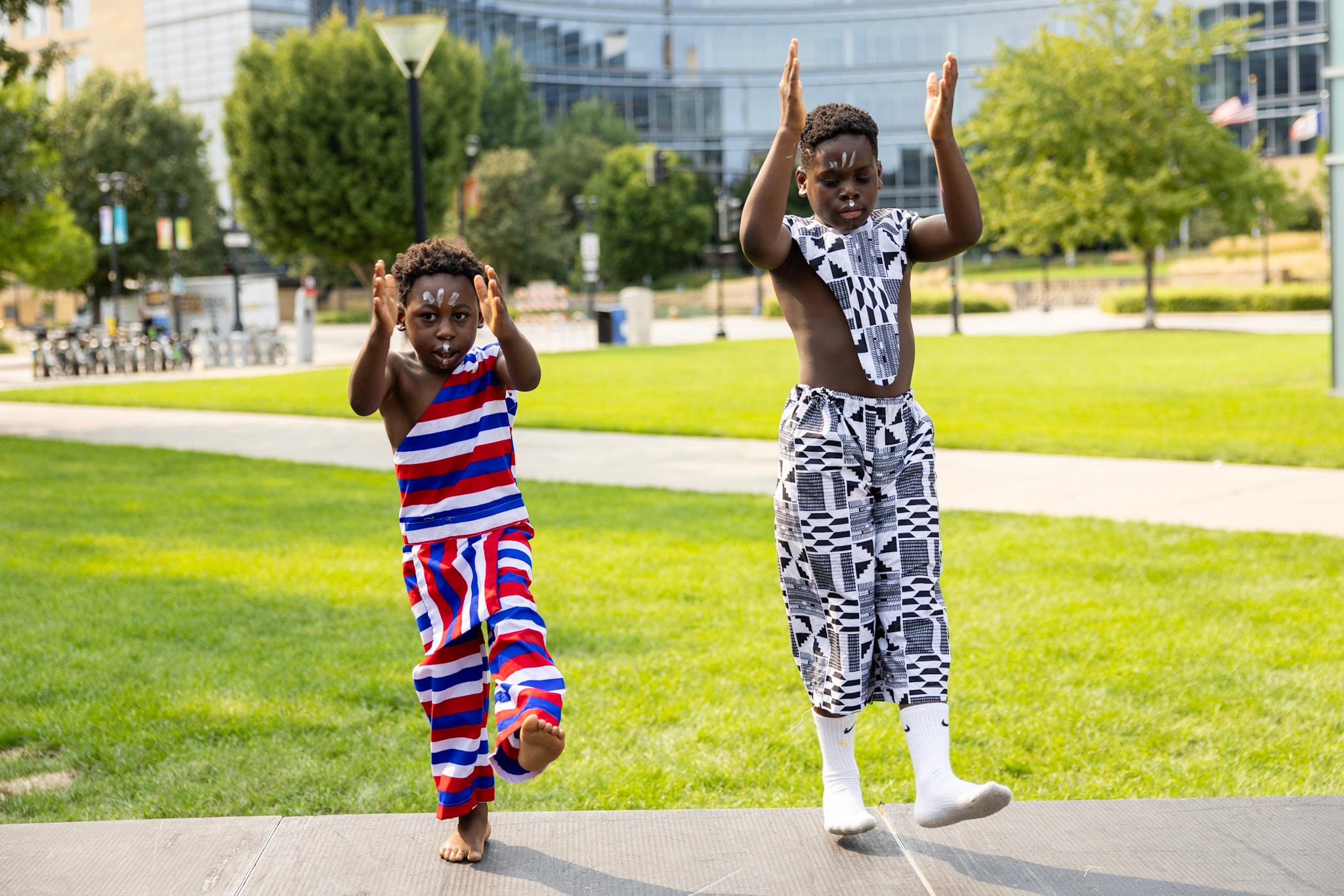 Two young boys in traditional kente and striped attire dancing at Western Gateway Park