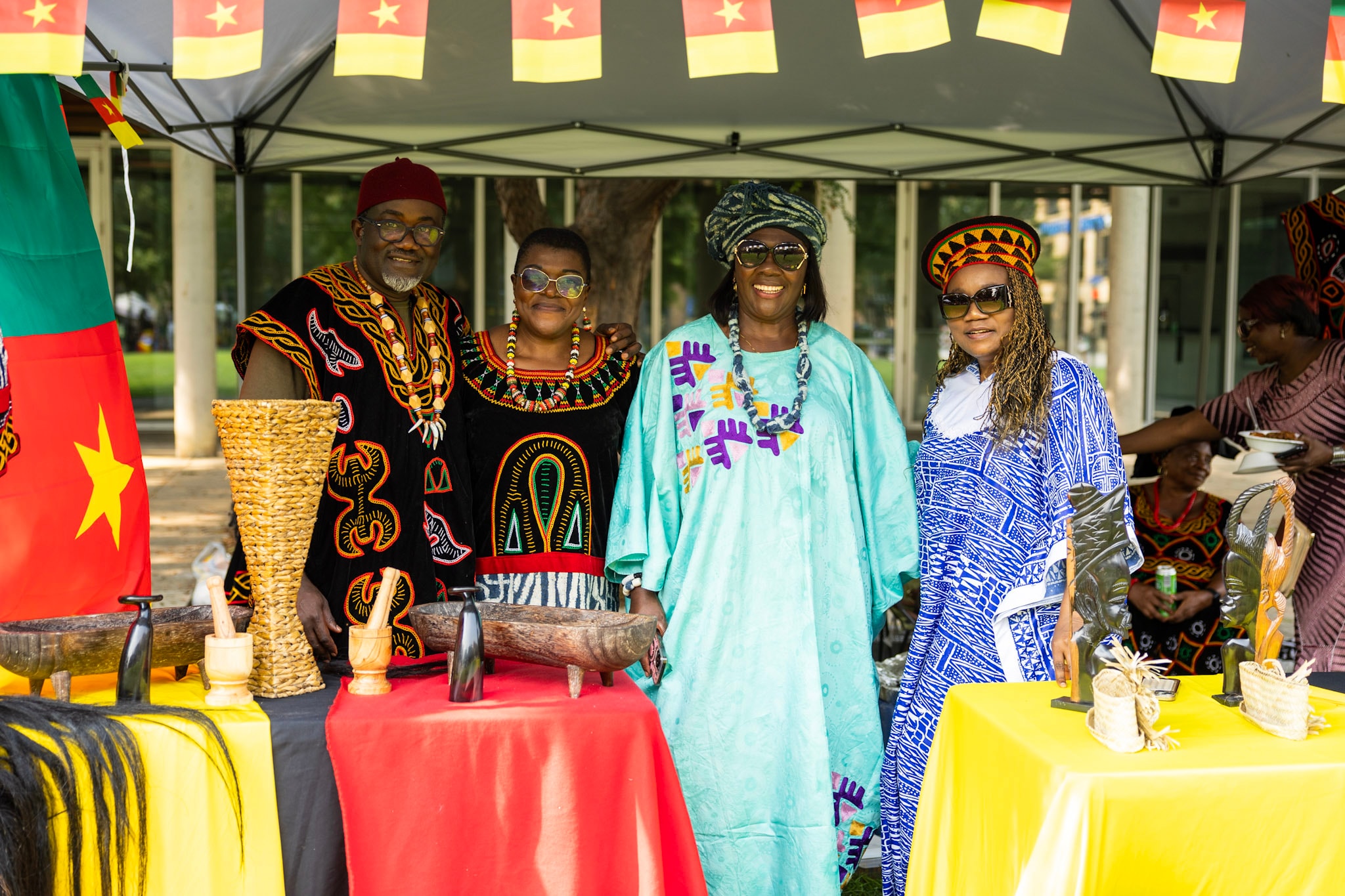 Four people in vibrant Cameroonian traditional attire at a cultural vendor booth