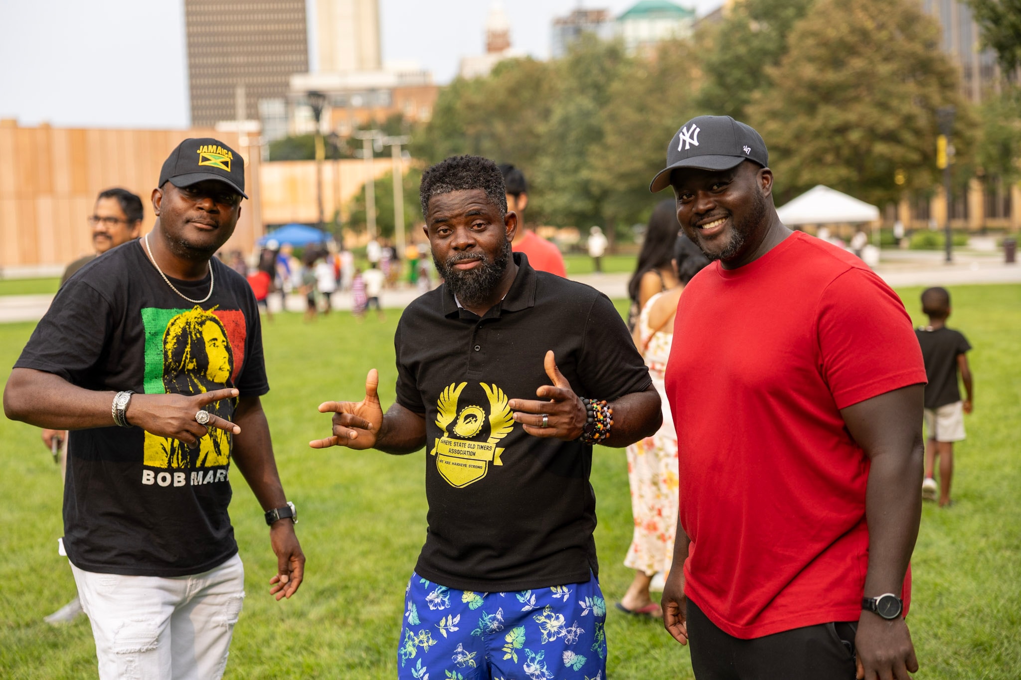 Three men smiling and posing together at the festival with the Des Moines skyline behind them