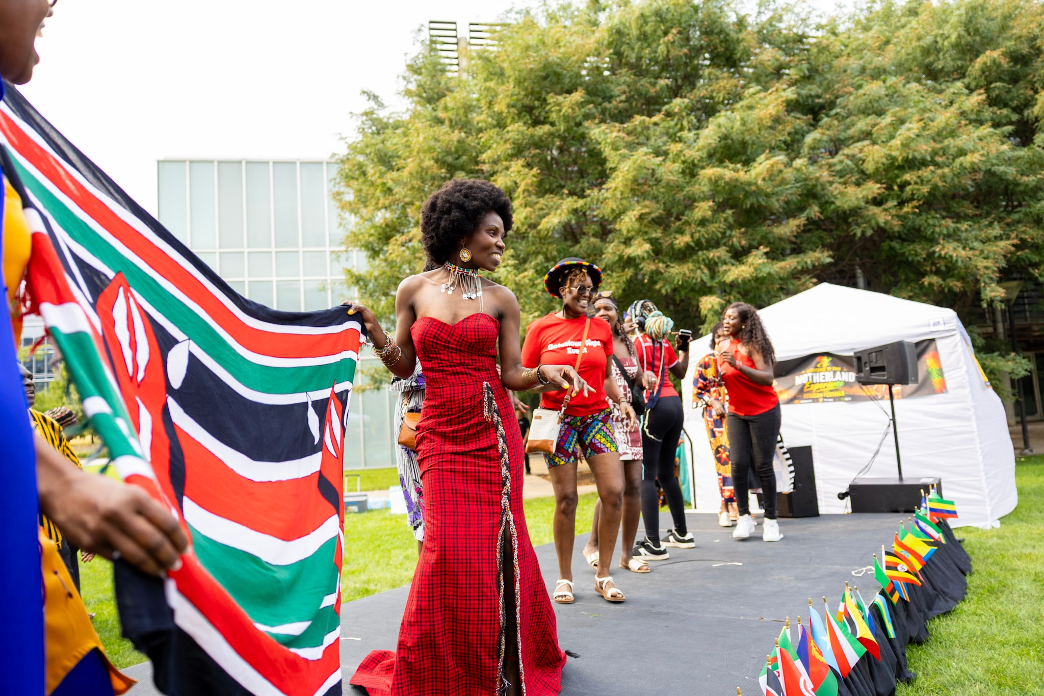 Woman in red dress walking the runway holding the Kenyan flag at the African fashion show