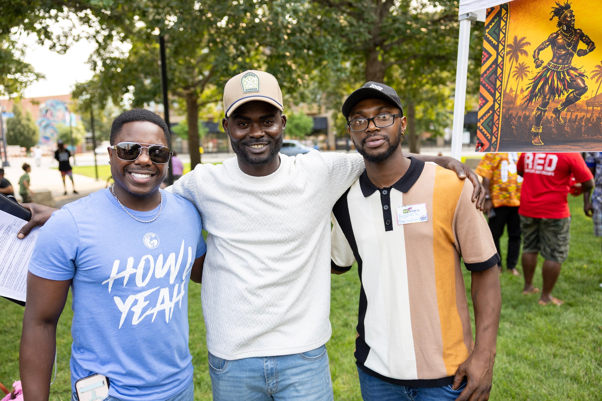 Three friends smiling together at the festival with cultural artwork in the background