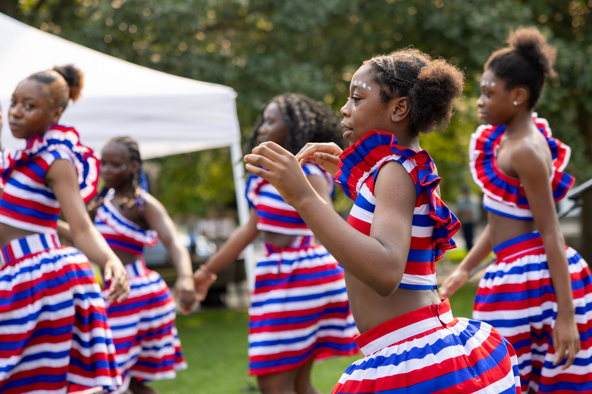 Young girls in red, white and blue striped outfits performing a cultural dance