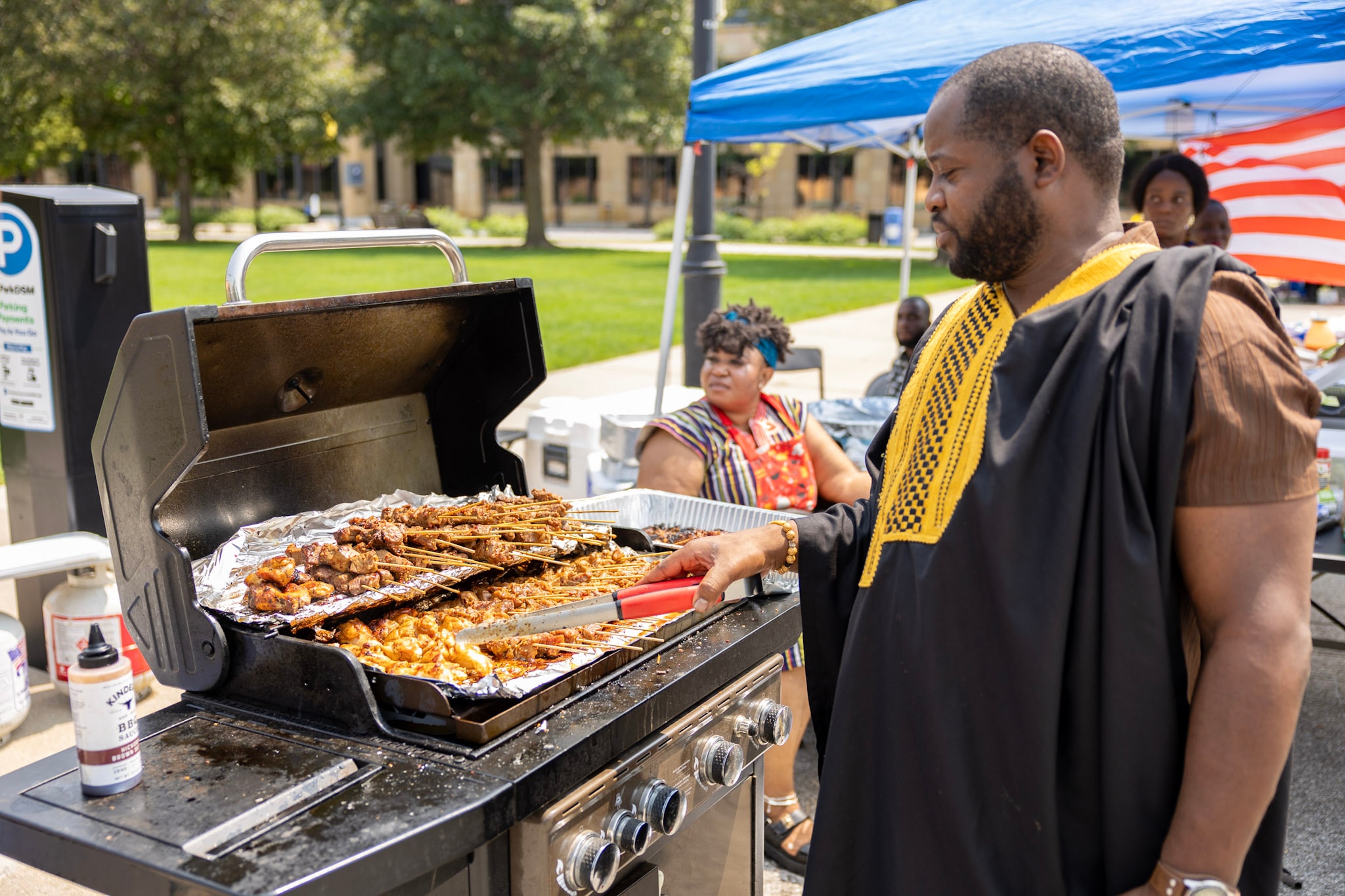 Man in traditional black and gold kente robe grilling skewers at the festival