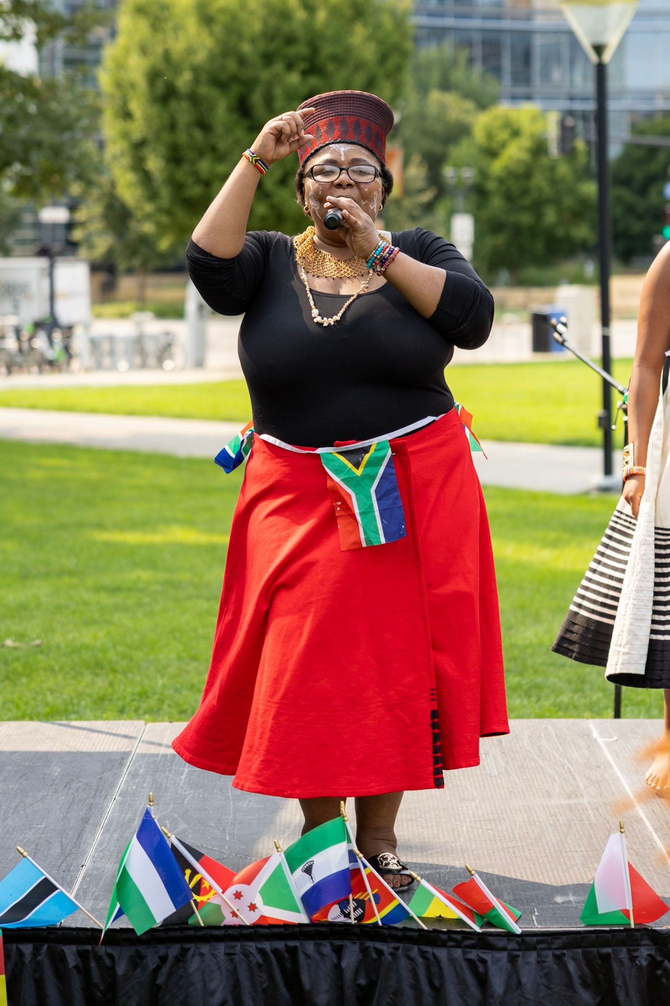 Woman in red skirt and traditional Zulu hat performing on stage surrounded by African flags