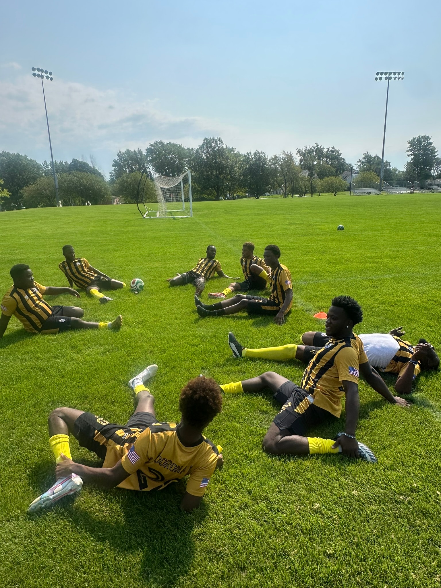 Soccer team in yellow and black uniforms relaxing on the field before the tournament