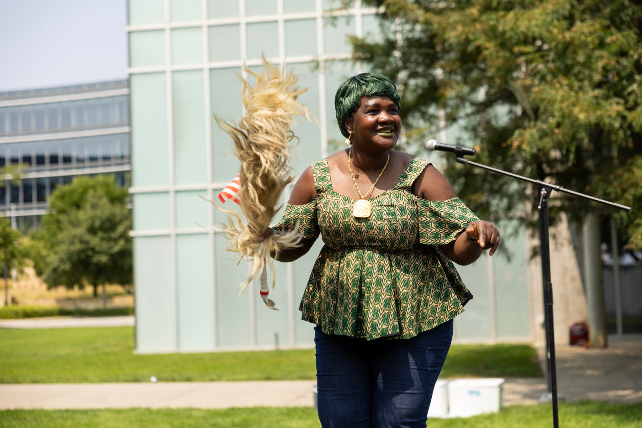 Woman in green African print top performing with a flywhisk at the festival microphone