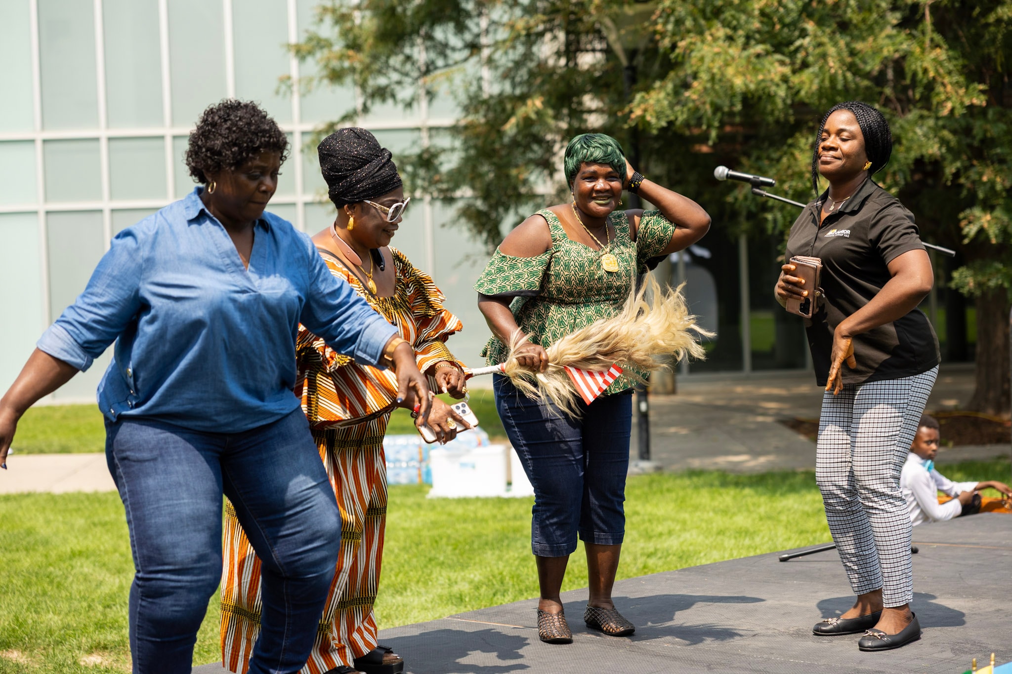 Four women laughing and dancing together on the outdoor stage at the festival